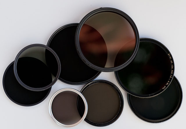 Neutral Density filters. ND (Neutral Density) filters to put in front of lenses to reduce the amount of light that comes in. They don't have any other effect than that and doesn't change contrast, color or anything.